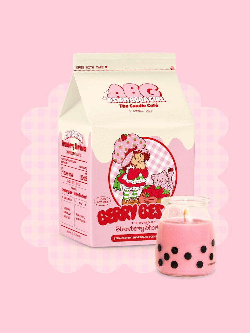 May include: A pink and white milk carton candle with a strawberry shortcake design. The candle is labelled "Berry Best" and "The World of Strawberry Shortcake". The candle is made with 100% soy wax.