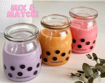May include: Three glass candle jars with black polka dots and a light pink, orange, and purple colored wax. The jars have the text "ASIANNOBAGIN" on the bottom.