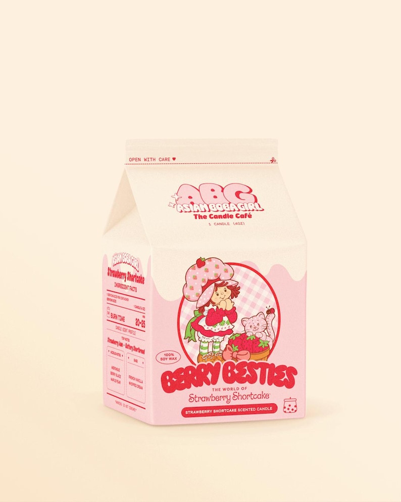 May include: A pink and white cardboard box containing a Strawberry Shortcake scented candle. The box features a cartoon image of Strawberry Shortcake and her cat, Berry Besty. The text on the box reads "Berry Besties The World of Strawberry Shortcake Strawberry Shortcake Scented Candle".