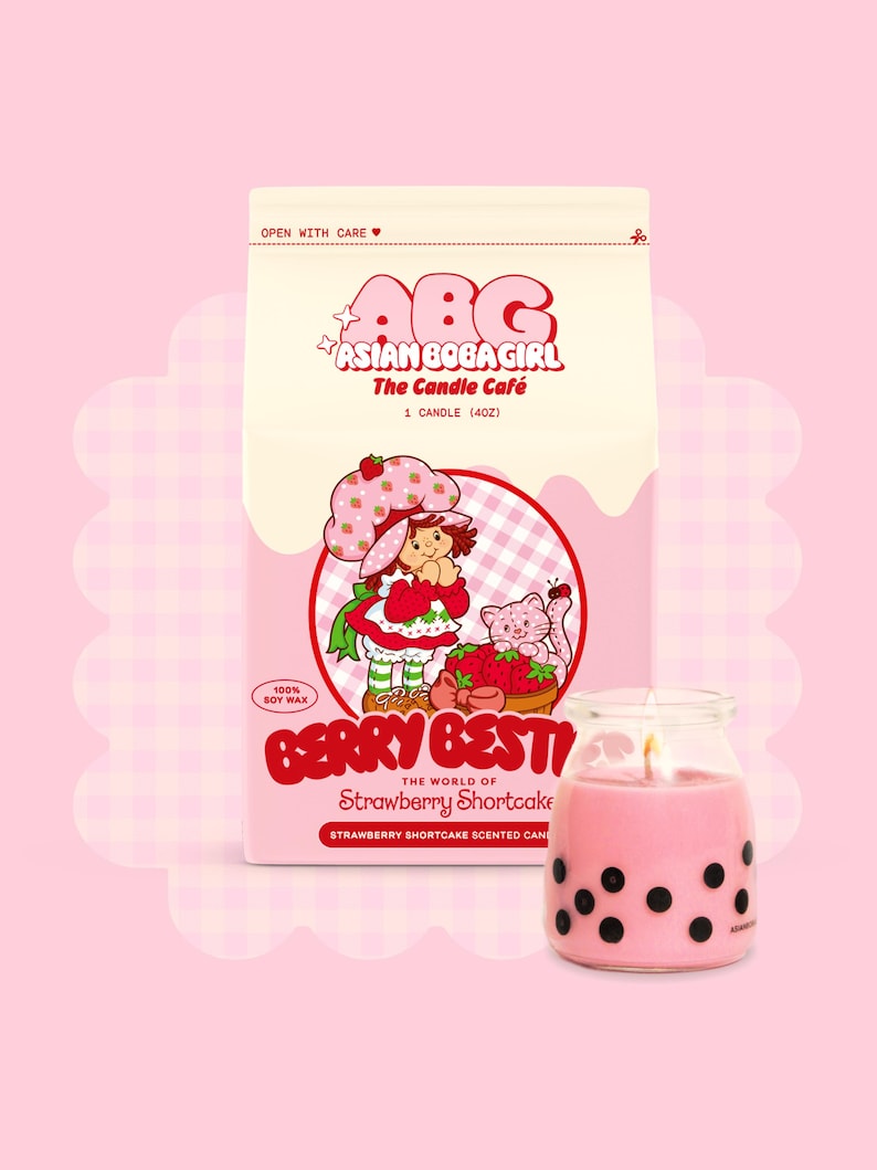May include: A pink and white candle jar with a black and white boba tea design. The candle is labelled "Berry Best" and "The World of Strawberry Shortcake". The jar is sitting on a white and pink background with a cartoon image of Strawberry Shortcake.