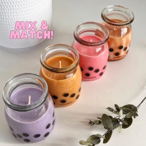 Op de afbeelding: Vier glazen potten met deksels, elk met een andere gekleurde kaars. De kaarsen zijn paars, oranje, roze en bruin. De potten hebben een zwart-wit stippenpatroon. De tekst "Mix & Match!" is geschreven in roze letters op een witte achtergrond.