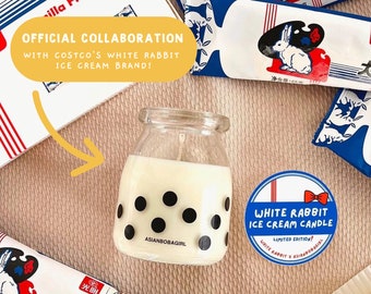 May include: A white milk glass candle with black polka dots and the text "ASIANBOBAGIRL" on the front. The candle is sitting on a pink surface with a white rabbit ice cream bar and a blue and white sticker that says "WHITE RABBIT ICE CREAM CANDLE LIMITED EDITION!"