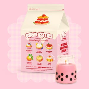 May include: A pink and black milk carton-shaped candle with a strawberry shortcake design. The candle is labelled "Berry Besties" and features different flavours of shortcake, including blueberry muffin, lemon meringue, raspberry tart, orange blossom, butter cookie, and angel cake. The candle is made with 100% soy wax and is hand-poured with love.