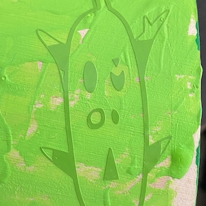 May include: Green painted wooden surface with a green silhouette of a cartoon character with a large head, two eyes, a nose, and a mouth. The character has two arms and two legs.