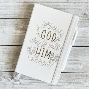 May include: White journal with a gold inscription that reads "To know GOD and to make HIM known" surrounded by floral designs.