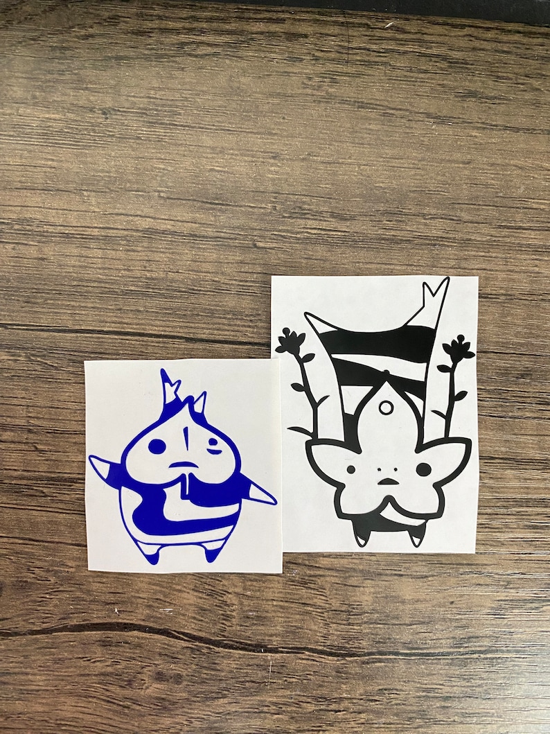 May include: Two black and white vinyl stickers featuring a cartoon character. The character is a creature with a large head, small body, and large eyes. The character is wearing a striped shirt and has a small mouth. The stickers are on a white background.