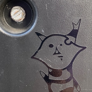 May include: Black and white sticker of a cartoon character with a crown on its head. The character is wearing a striped shirt and has a large, round head.