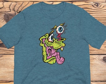 Peut inclure: Un t-shirt bleu sarcelle avec une illustration de dessin animé d'un monstre vert avec une langue rose et un seul œil bleu.