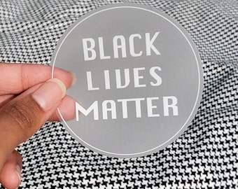 May include: A clear round sticker with the text "BLACK LIVES MATTER" in white lettering.