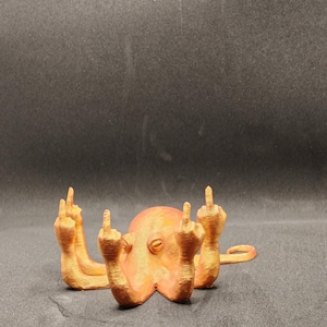 Könnte beinhalten: Eine orangefarbene 3D-gedruckte Tintenfischfigur mit allen acht Tentakeln in einem Mittelfinger-Gestus erhoben.