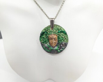 May include: A silver chain necklace with a round pendant featuring a woman's face with green hair and a black and brown background.