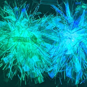 K&ouml;nnte beinhalten: Zwei schimmernde blaue und gr&uuml;ne Pompons mit einer silbernen Kette, die von oben h&auml;ngt.