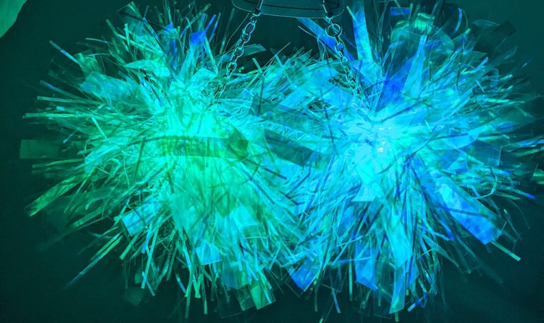K&ouml;nnte beinhalten: Zwei schimmernde blaue und gr&uuml;ne Pompons mit einer silbernen Kette, die von oben h&auml;ngt.