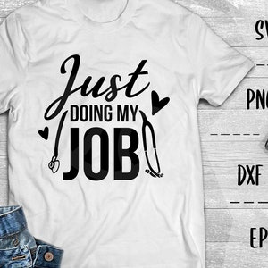 Op de afbeelding: Wit T-shirt met zwarte tekst die "Just Doing My Job" luidt en een stethoscoopgrafiek.