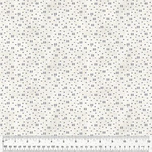 May include: Cream-colored fabric with a repeating pattern of small, dark blue geometric shapes and dots. A ruler is at the bottom, showing measurements in inches. The fabric has a subtle texture.