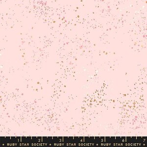 May include: Pink fabric with a speckled design. The fabric features a light pink background with scattered gold, pink, and white dots. The bottom of the fabric has a black ruler with the text "RUBY STAR SOCIETY".