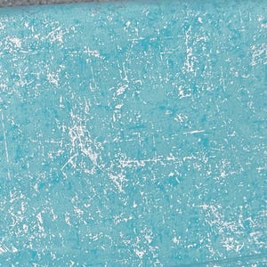May include: A close-up of a textured, turquoise fabric with a distressed, white, scratch-like pattern. The fabric has a subtle, woven appearance, and the white markings are irregularly distributed across the surface.