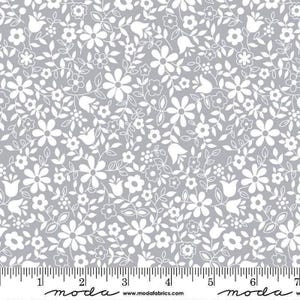 May include: Gray fabric with a white floral pattern. The design features various flower shapes, including daisies and tulips, along with leaves and small buds. A ruler is at the bottom, with the word "moda" and website address printed on it.