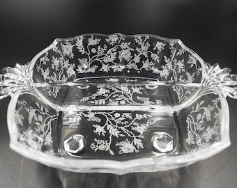 May include: A clear glass divided serving dish with a floral design etched into the glass. The dish has a scalloped edge and three feet.
