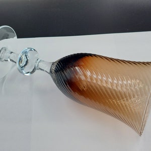 May include: A clear glass wine goblet with a brown and amber swirl design. The goblet has a wide base and a long, slender stem.
