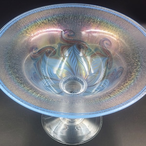 May include: A clear glass bowl with a blue iridescent rim and a swirling blue and brown design on the inside. The bowl is on a clear glass pedestal.
