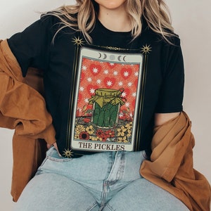 May include: A black t-shirt with a graphic of a tarot card featuring a jar of pickles and the text "THE PICKLES".