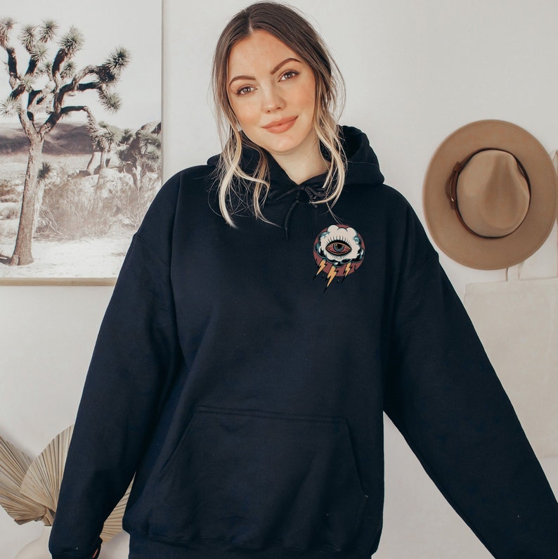Op de afbeelding: Een zwart hoodie met een afbeelding van een oog in een wolk met bliksemstralen op de voorkant.