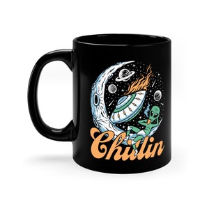 May include: Black coffee mug featuring a graphic of an alien relaxing on a crescent moon with a UFO and the text "Chillin".