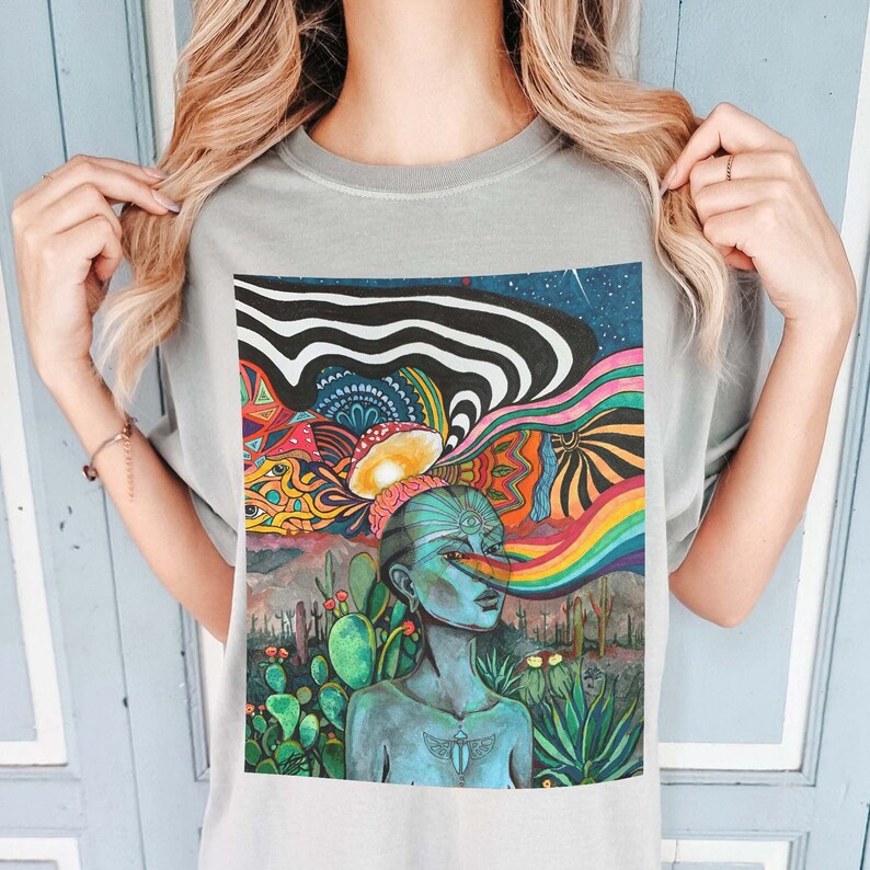 Puede incluir: Una camiseta gris con un dise&ntilde;o psicod&eacute;lico colorido que presenta a una persona con un tercer ojo y un arco&iacute;ris. El dise&ntilde;o incluye cactus, hongos y un patr&oacute;n de remolino.