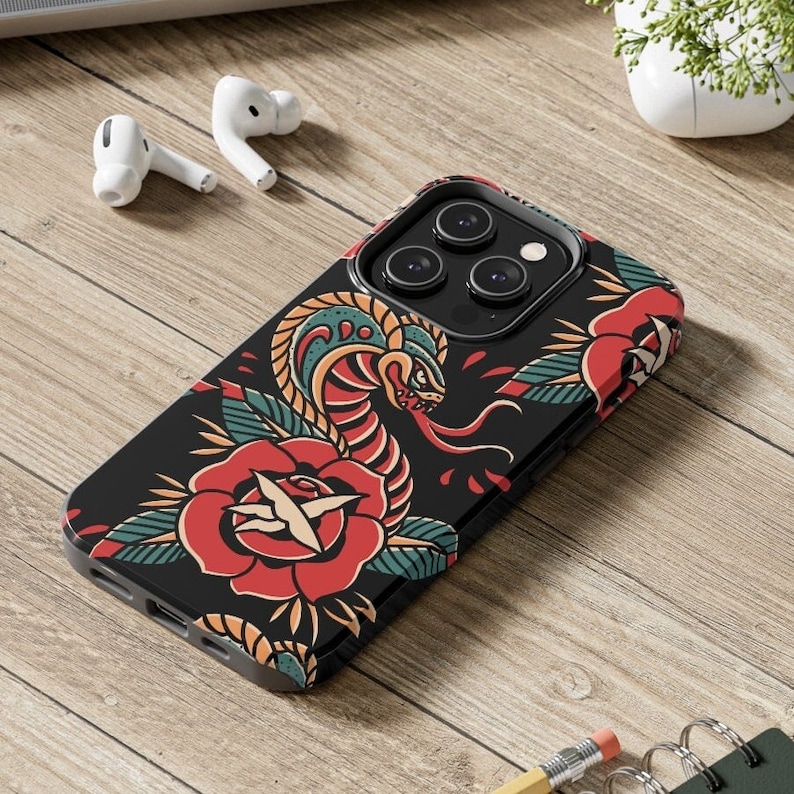 May include: Black phone case with a colorful tattoo-style design featuring a snake and a rose. The case has a camera lens cutout and a black border.