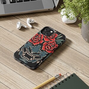 May include: Black phone case with a graphic design of a red and green floral pattern and a blue and white demon face.