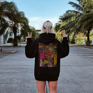 Puede incluir: Una sudadera con capucha negra con un estampado gr&aacute;fico colorido en la espalda. El gr&aacute;fico presenta un grupo de personas con patrones psicod&eacute;licos y una persona con un tercer ojo.