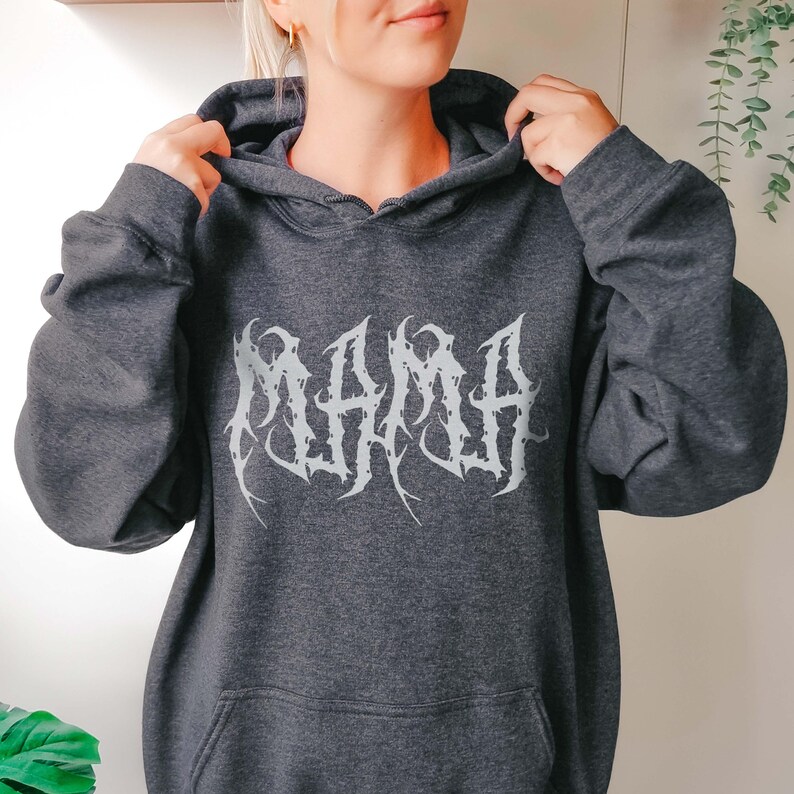 Puede incluir: Sudadera con capucha gris oscuro con la palabra "MAMA" en una fuente g&oacute;tica blanca en el pecho. La sudadera con capucha tiene una capucha con cord&oacute;n y un bolsillo delantero. Las mangas son largas y el material parece ser una tela suave y c&oacute;moda.