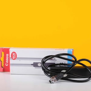 May include: A black Canon EOS remote shutter release cable with a white button and a black box. The cable is coiled and the box is labeled "Canon EOS".