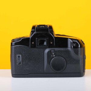 Puede incluir: Una c&aacute;mara de pel&iacute;cula Canon negra con una lente y un dial en el lateral.