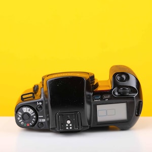 Puede incluir: Una c&aacute;mara de pel&iacute;cula negra con una pantalla digital. La c&aacute;mara tiene varios botones y diales.