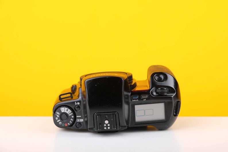 Puede incluir: Una c&aacute;mara de pel&iacute;cula negra con una pantalla digital. La c&aacute;mara tiene varios botones y diales.