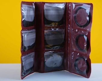 May include: A burgundy leather case with clear plastic pockets for storing camera filters. The case is open and shows a variety of filters in different sizes.