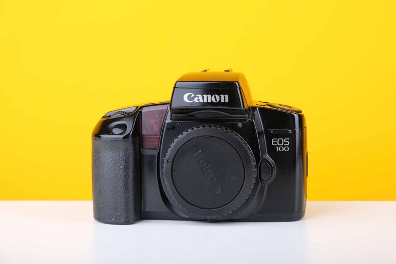 Puede incluir: Una c&aacute;mara de pel&iacute;cula Canon EOS 100 negra con una tapa de lente.