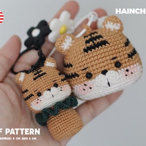 May include: Two crocheted tiger keychain charms, one with a green bow. The charms are approximately 5 cm and 6 cm tall. The image includes the text "PDF PATTERN" and "HEIGHT APPROX: 5 CM AND 6 CM".