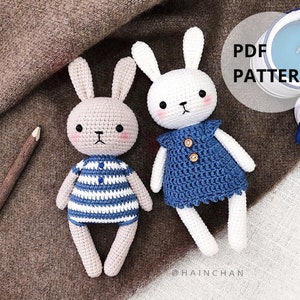May include: Two crocheted bunny amigurumi toys. One bunny is white with blue and white striped clothing. The other bunny is beige with blue and white striped clothing. The text "PDF PATTERN" is visible in the image.