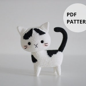 Pode incluir: Padrão de crochê para um amigurumi de gato preto e branco. O padrão está disponível para download em PDF.