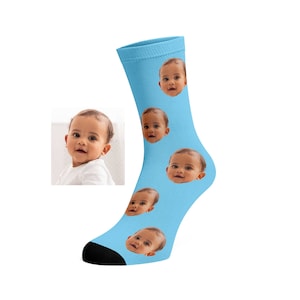 May include: Light blue sock with multiple baby face images. The sock has a black heel and toe. The baby's face is repeated multiple times on the sock.