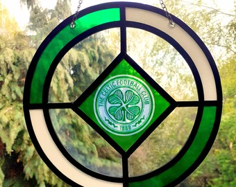 Puede incluir: Vidriera con el logotipo del Celtic Football Club. El diseño incluye un emblema de trébol verde dentro de un rombo, rodeado por un borde circular verde y blanco, y el texto "THE CELTIC FOOTBALL CLUB 1888".