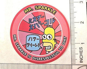 May include: A circular sticker featuring a yellow cartoon character with wide eyes, a pink sunburst background, and the text MR. SPARKLE, MR. SPARKLE IS DISRESPECTFUL TO DIRT, and Japanese characters. A ruler shows the sticker is approximately 2.5 inches wide.