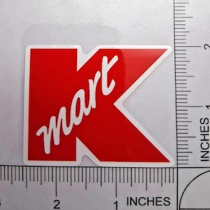 May include: A red Kmart logo sticker with white text that reads "mart". The sticker is approximately 2 inches wide and 2 inches tall. The sticker has a white border.