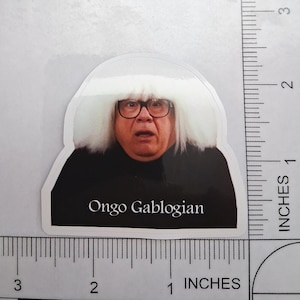 May include: A sticker featuring a portrait of a man with glasses and a white wig, with the text "Ongo Gablogian" below. The sticker is approximately 2 inches tall.