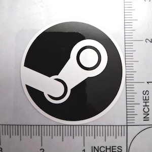 May include: A round, black and white sticker featuring the Steam logo. The logo consists of a white gear-like shape inside a black circle. The sticker is approximately 2 inches in diameter.