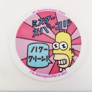 May include: A round sticker with a pink and white background. The sticker features a cartoon character with yellow skin, a large smile, and three eyes. The character is saying "Hi-ya!" in Japanese. The sticker also has the text "Mr. Sparkle Power Clean" and "I'm Disrespectful to Dirt".