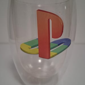 May include: Clear double-walled glass with a colorful logo. The logo features a red letter "P" above a stylized blue, green, and yellow shape. The glass has a rounded, oval shape.